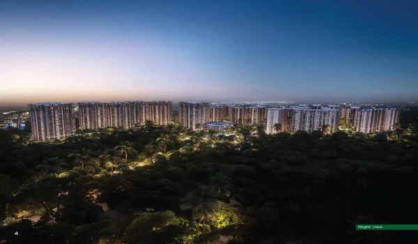 A wide aerial night rendering of the Sattva City apartment project in North Bangalore. The high-rise towers are warmly lit against a deep blue dusk sky, overlooking a vast, dark green forest area. Soft landscape lighting accentuates the pathways and trees within the complex, creating a glowing, high-end residential atmosphere.